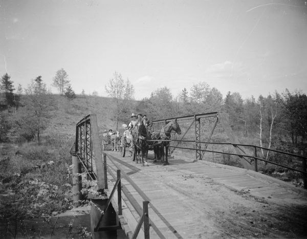 Carriages Crossing Bridge Several families in carriages cross a bridge with a high railing, possibly the Levi Creek Bridge.