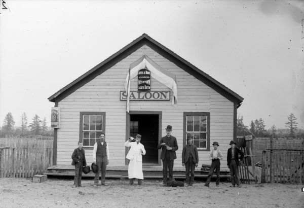 Bartender and six patrons posing in front of a saloon. The saloon sign reads: "Celebrated Watertown Lager Beer."