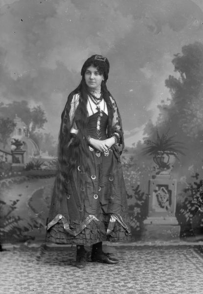 Portrait of a Fortune Teller A studio portrait of a woman dressed as a fortune teller in front of a painted backdrop. She has long, loose hair and is wearing a dress.