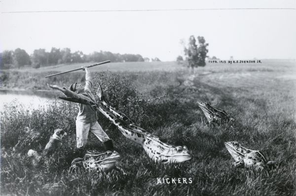 Photomontage of a group of giant frogs next to a pond. One of the frogs is kicking a boy's arms, causing them to fly upwards. A dog is sitting by the feet of the boy. A pond is visible behind them. The word, "Kickers," appears in white text at the bottom.
