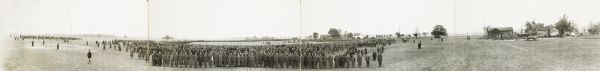 Panoramic view of the 8th Division Field Meeting at Camp Custer. Hundreds of soldiers in overcoats and hats with a wooden wall used for training visible in middle ground.
