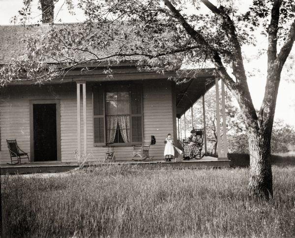 Ada Bass sitting in a rocking chair reading, while her daughter Everetta is sweeping the front porch of the family home.