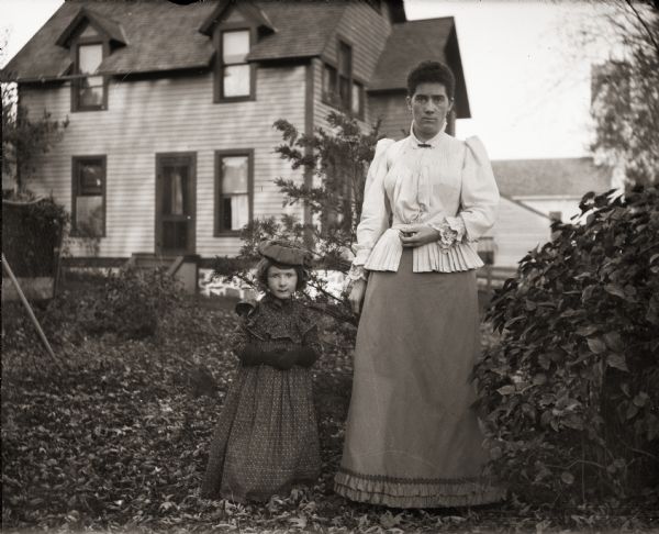 Everetta Bass standing next to a woman identified as Llora. They are standing in front of a house at 131 East Montello Street, with the Methodist Church, located at 147 East Montello Street, in the background.