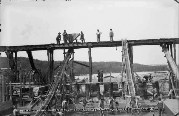 Workmen pouring concrete from the elevated railroad into forms below.