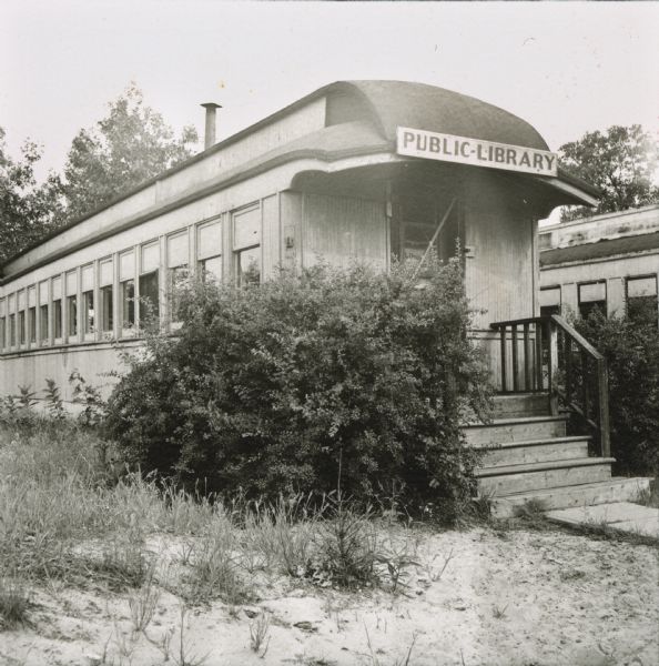 Public Library housed in a stationary railroad car in Adams, WI. The train car was a gift from F. W. Sargent of the North Western Road at the request of Mrs. J. F. Duncan and Mrs. Pearly Bennett of the Adams Library Association.  Mrs. Hazel Fease worked to make the train car into a subscription library.