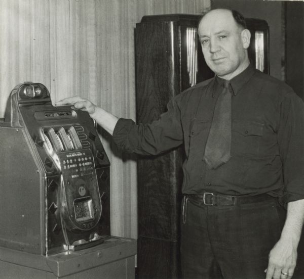 Frank Deischel, Wausau, President of the Tavern League of Wisconsin,  standing with an illegal slot machine in Deischel's tavern.