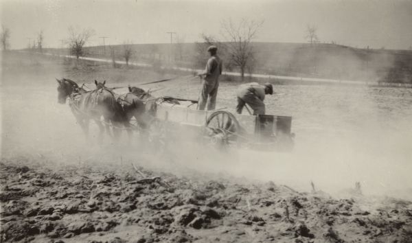 In a cloud of dust, two farmers spread lime on the field of C. Morris, Green Lake, with an endgate spreader drawn by a team of horses.