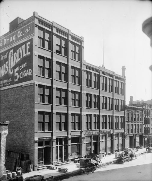 Elevated view of the Yahr and Lange Drug Company on N. Water Street between E. Erie and E. Chicago Streets. There are horse-drawn vehicles parked in front of the building.