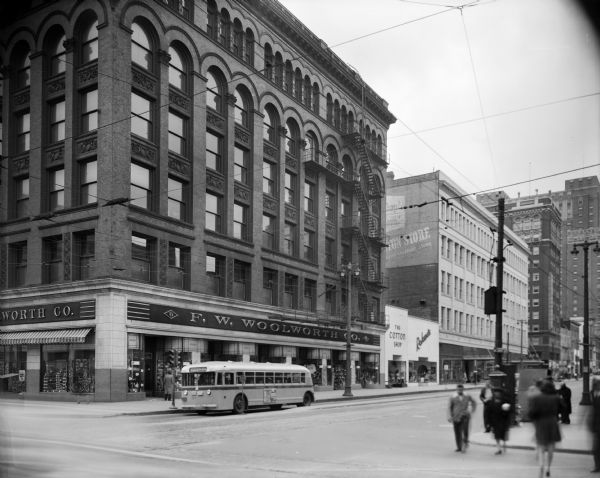 Looking west on W. Wisconsin Avenue from N. 3rd Street, featuring Woolworth's, Boston Store, and the Schroeder Hotel. An Edgewood-bound bus is stopped in front of F.W. Woolworth Company.