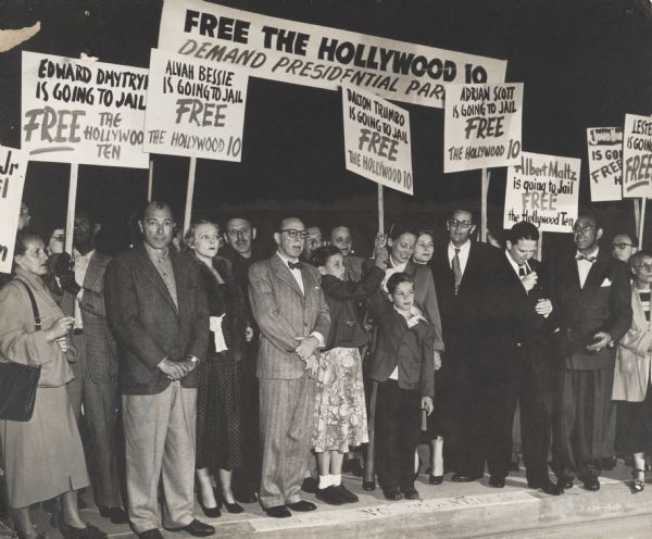 Several members of the screenwriters and directors known as the "Hollywood Ten," together with members of their families at a demonstration before their imprisonment for failure to testify before the House Un-American Activities Committee about their Communist Party memberships or associations. Included second from the left are Albert Maltz, Alvah Bessie (in the beret), and Dalton Trumbo (wearing eyeglasses). Herbert Biberman is third from the right and Ring Lardner, Jr., is standing under the Adrian Scott sign. Public concern that Communist sympathizers might be including propaganda in Hollywood films was part of the background to the anti-Communist hysteria created by Joseph R. McCarthy during the 1950s.