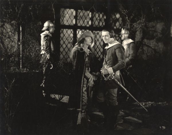 A scene still from <i>The Fighting Blade</i> with Richard Barthelmess and Dorothy Mackaill in the foreground and two helmeted guardsmen behind them.