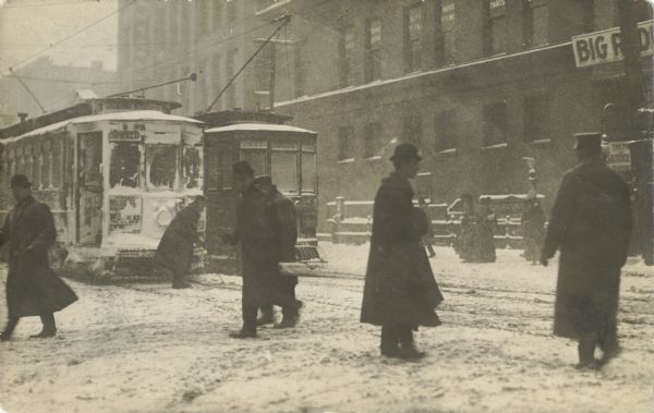 Snow covers a streetcar and pedestrians walk through a snow-covered street.