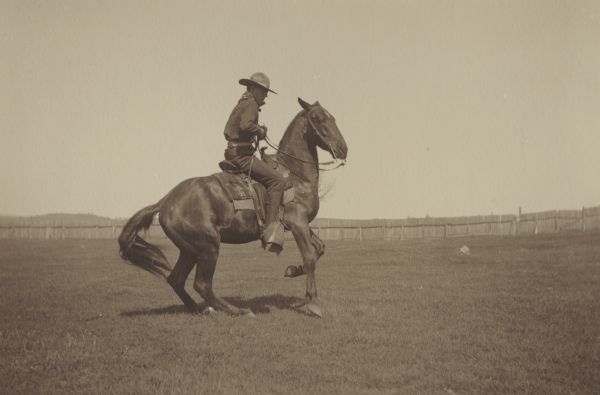 George E. Thompson, member of the Menomonie High School class of 1905, depicted as a cowboy. Pictured riding a horse and wearing a cowboy hat. Part of a yearbook created by classmate Albert Hansen, based on a class prophecy theme.
