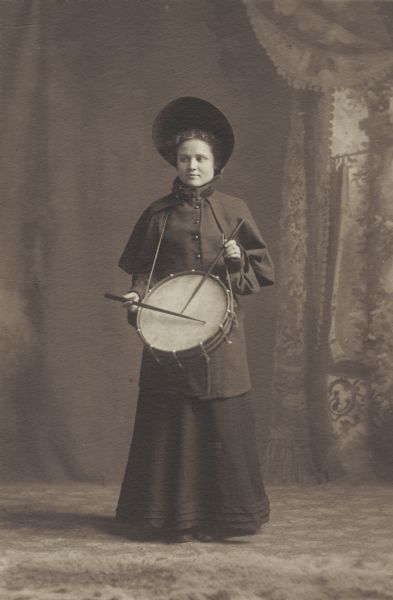 Eva Charlotte Cook, member of the Menomonie High School class of 1905, depicted as a drummer for the Salvation Army. Pictured with a large bonnet and a drum. Part of a yearbook created by classmate Albert Hansen, based on a class prophecy theme.