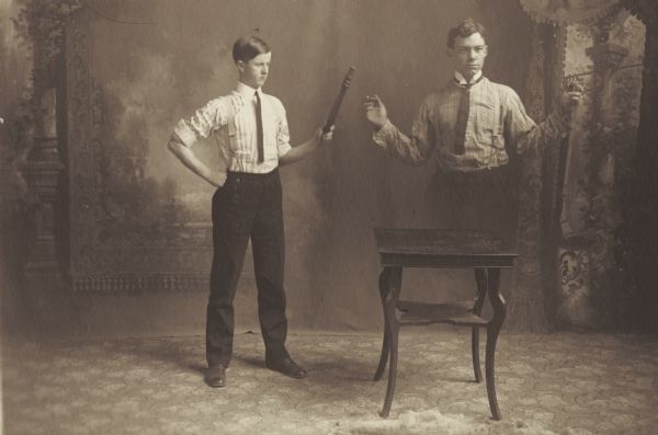 William R. Holmes, member of the Menomonie High School class of 1905, depicted as a professional magician in front of a painted backdrop. Pictured with a magic wand that resembles the leg of a chair, causing an assistant to disappear. Part of a yearbook created by classmate Albert Hansen, based on a class prophecy theme.