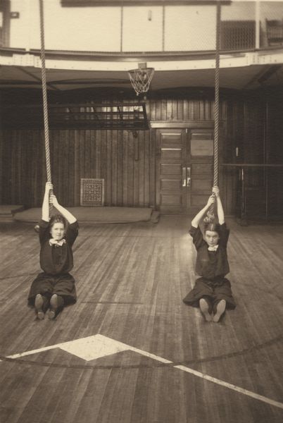 Hazel Andersen with her friend Lucile Wilcox, both members of the Menomonie High School class of 1905, depicted as gymnasts, holding on to climbing ropes. Part of a yearbook created by classmate Albert Hansen, based on a class prophecy theme.