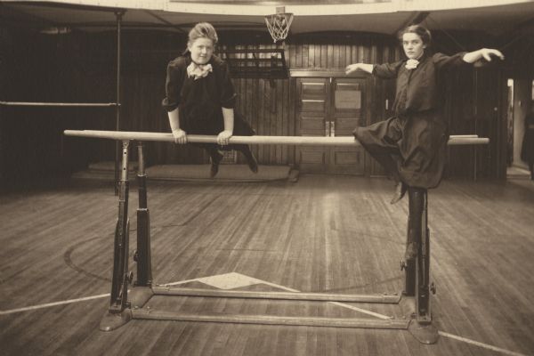 Lucile Wilcox with her friend Hazel Anderson, both members of the Menomonie High School class of 1905, depicted as gymnasts, on a set of parallel bars. Part of a yearbook created by classmate Albert Hansen, based on a class prophecy theme.