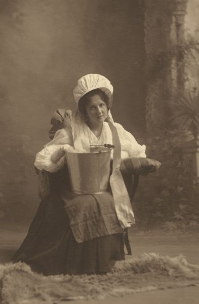 S. Ana Heller, member of the Menomonie High School class of 1905, depicted as an unclear profession, putting a piece of paper or cloth in a bucket. Part of a yearbook created by classmate Albert Hansen, based on a class prophecy theme.