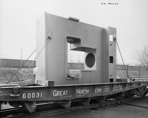 A seamless pipe fitting sits atop a railroad car, ready to be shipped. Later purchased and used by Elmes & Kings. Original Falk caption reads: "14' high-78,000 pound rgh unit."