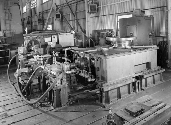 Pulverizer Mill A male employee, Don Ferch, attends to a pulverizer mill. This unit was purchased by the Foster Wheeler Energy Corporation and used by the Public Service of Indiana Unit number 1. This specific pulverizer mill was a later component of a coal pulverizer. Original Falk caption reads, "This is a customer's standard unit. 537 HP with input at 870 RPM, ratio 27.83:1, output speed 31.26. Service factor 2.0, double ratio with 4.062 spiral bevels as first reduction, single helicals as second reduction (6.85:1 ratio). Anti-friction bearings throughout. Low speed thrust bearing is a special spherical roller SKF294/630. ALl other bearings are tapered roller bearings. Pressure lube system and cooling, oil filtering, oil metering is provided with each unit. Turning gear arrangement is provided for each set of units (such as six). Photos show hydraulic pump and motor system for testing the unit at full speed but no load. Six units are on this order."