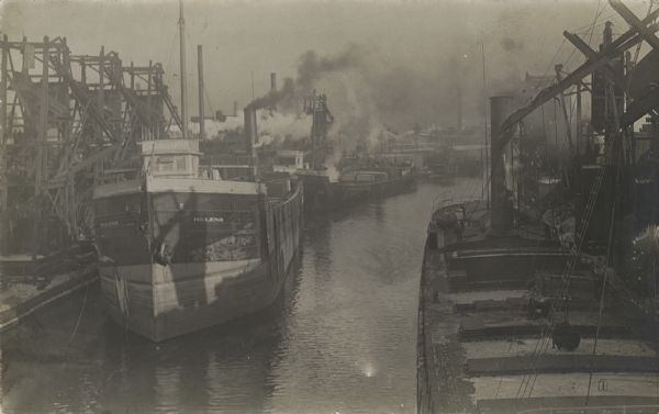 Canal with several ships, mostly small steam-engine cargo ships.