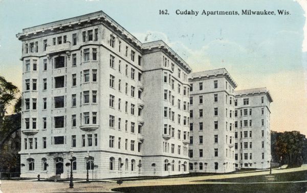 Exterior of Cudahy Apartments with a road in front and along the side of the building, with lamposts, and trees in the background. Caption reads: "Cudahy Apartments, Milwaukee, Wis."