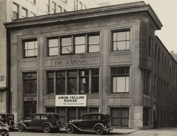 The newspaper used this building from 1907 until the mid or late 1920's. A few cars are parked in front of the building. A sign for the Good Fellow House (operated by the Salvation Army) is on the front of the building.