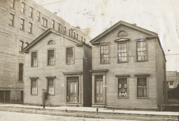 First location of the high school at 301-303 Fifth Street. Consists of two house-sized buildings, with the entrances close to each other. Sign on front of building at left says: "Furnished Rooms for Rent," and sign on door near right says: "Furnished Rooms."