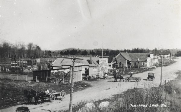 Lumbertown Street (Now Highway 47). There are horse-drawn carts and a car.  Sailors burned down Lumbertown in 1897. It was later built up as a resort town. A restaurant and an auto livery are some of the buildings along the road.