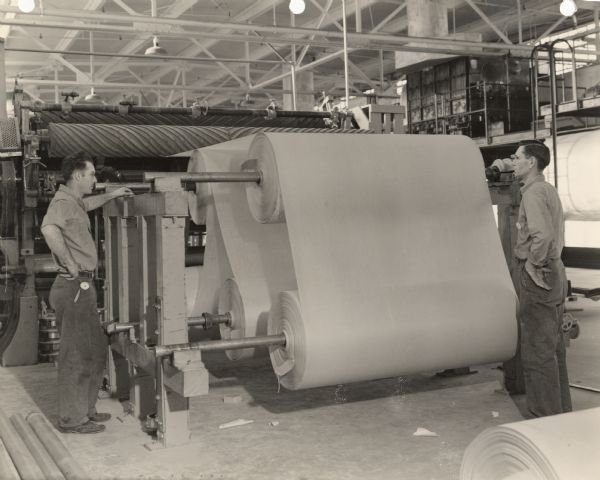 Two employees, Bob Schutz and Louis Timmerman, watch as rolls of stock are cut five sheets at a time.  This procedure was necessary to insure uniformity of weight and thickness of the laminate product the company manufactured for use in the production of military gliders during World War II.
