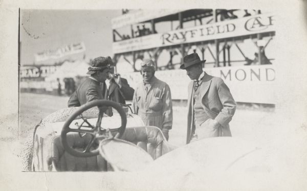 Bob Burman, left, leans on a #31 Benz race car. Caleb Bragg, winner of Grand Prize Race in 1912, on road course in Wauwatosa, faces the camera. The other two men are unidentified. An observation area for viewing the racing is in the background.