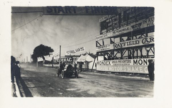 Teddy Tetzlaff drives the Fiat #33 across the finish line. The stands on the right are covered in advertisements. The track later became Burleigh Street going east.