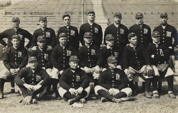 Group portrait of the Milwaukee Brewers of the American Association on a field with a stadium in the background. Some of the players have their gloves with them. The catcher is sitting on the bench on the right.