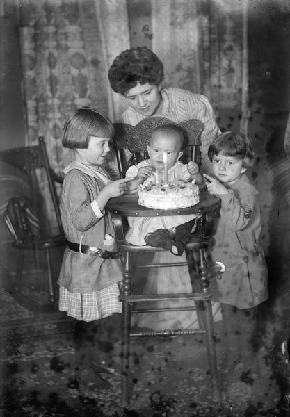 The J. Robert family posed around baby Fred in a high chair with his first birthday cake.  Family members are identified from left as Ellen Taylor Higgins, Fred Taylor, Alma Reinhardt Taylor, and Donna Taylor Adams.