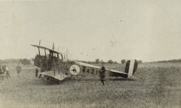 Side view of a Curtiss JN-4 "Jenny" airplane / biplane parked in a field (probably Weber Farm south of Lake Monona) with onlookers nearby.  Airplane has a black cat symbol in a circle and the number 44214 or 44216 on the side. Titled in the album "The First Aeroplane in Madison". "The feature of the flight was the delivery of a letter to Postmaster Devine from Pres. William F. Brooks of the Minneapolis Aero Club.  This is the first aerial letter ever received in Madison and the first aerial postage stamp ever received here.  The flyers are returning from a 3,000 mile run and have been making exhibition flights at state fairs."  The Capital Times 9-4-1918.One of five airplane images taken over a two day period.