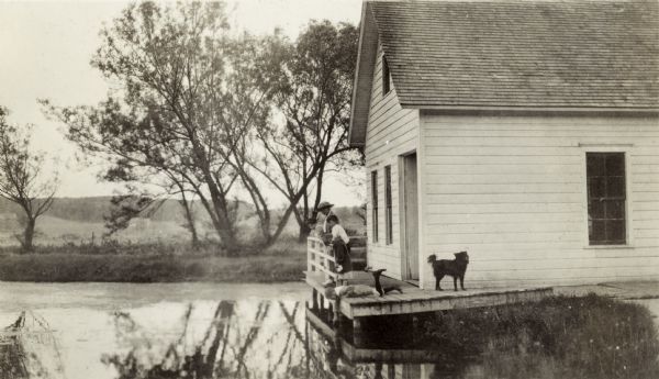 Members of the Richard Lloyd Jones family and their dog on a pier behind the building overlooking a pond at the Wisconsin State Fish Hatchery (aka Nevin Fish Hatchery, 3911 Fish Hatchery Road), south of Madison.