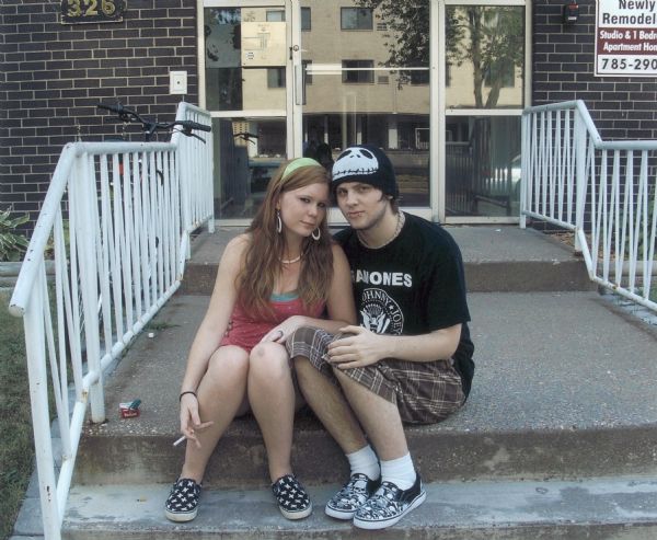 Portrait of a young woman, Crystal, and her friend, sitting on the steps of 326 South 7th Street. The friend is wearing a Ramones t-shirt, a hat, and shoes adorned with skulls.