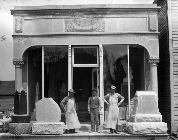 The storefront of Nicholas Kettenhoffen's "Graves Stones & Markers." Three men are standing in front of the store with three large grave markers.