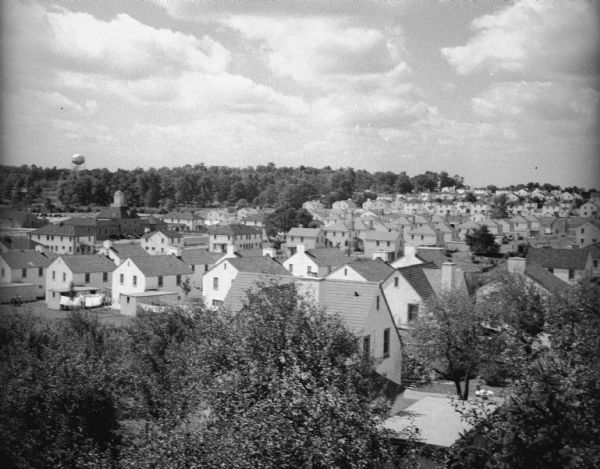 Elevated view over trees of village. In the background is a water tower on a hill with trees.