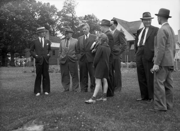 Henry Wallace meeting with a number of men and one young girl. A garden and residences can be seen in the background. Henry Wallace, then the United States Secretary of Agriculture, visited and toured Greendale.