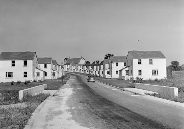 View down road of mass-produced residential housing with farm in background.
