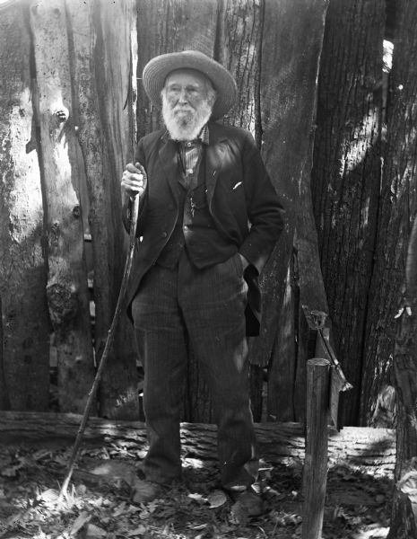 William H. Canfield, an early settler of Sauk County, civil engineer, local historian and archeologist, posing outdoors holding a walking stick.