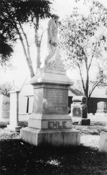 A very large cemetery monument with a female figure sculpture, inscribed with the name Ehle.  There is a shed in the background.  The Ehle family lived in an old tavern at Plymouth.