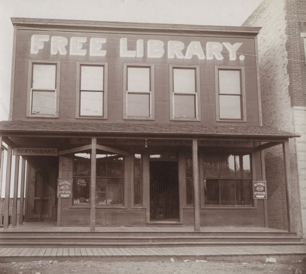 Exterior view of the Wausaukee Public Library. Above the windows on the second floor is painted: "Free Library" in large letters. Two signs advertise: "Booth's Oysters." The wooden two-story building has an open porch. There is a restaurant on the first floor.

Additional notes from "Some Wisconsin Library Buildings, 1904."
Established 1902. 1,000 volumes. This "social hall" was given by Hon. H. P. Bird as an attempt at the solution of the social problem of a small lumber town. The building contains library, reading-room. lunch and dining room, and amusement room.