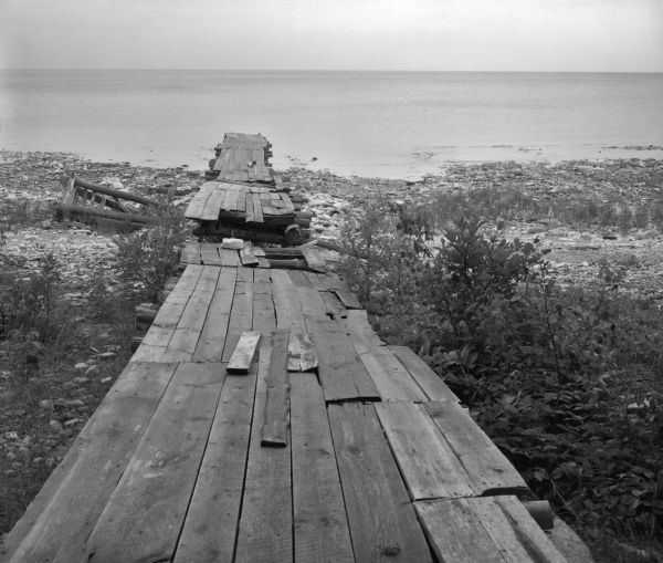 Dilapidated Boat Dock View towards horizon of old boat dock extending into Lake Michigan, as seen from the West Harbor of Washington Island. The dock is surrounded by plants and large gravel.