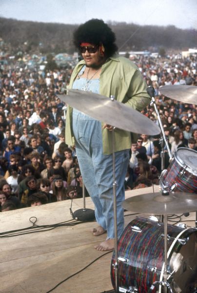 Chicago R&B singer Baby Huey standing barefoot on stage wearing an open green shirt on top of coveralls. A drum set and cymbals are visible on the right side of the photograph, and a large crowd is in the background.
