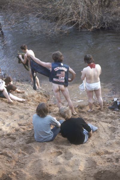 Bikers wash on the bank of Rowan Creek near York Farm during the Sound Storm music festival. One of the bikers is naked from the waist down and wearing a denim jacket with the words "Windy City M.C. Chicago." Another biker is wearing only a white pair of underwear and a red bandanna around his neck.