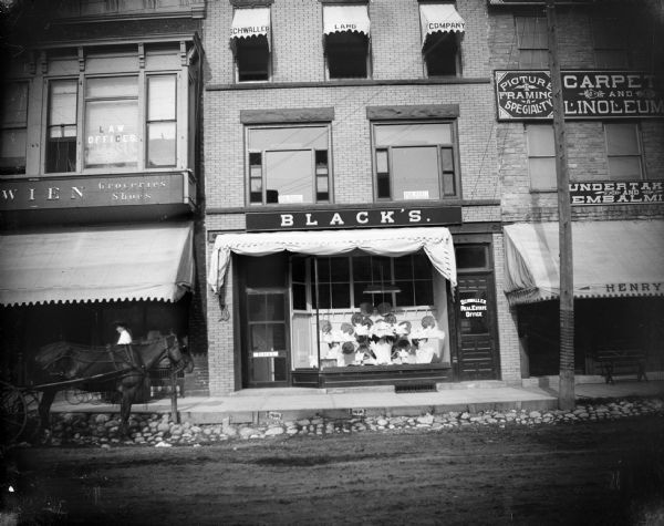 Looking east across Pine Street at Jacob Black's dry goods store, with a display of hand fans in front window; Schwaller's Real Estate company is above Black's. A horse-drawn carriage is near the sidewalk on the left.Schwaller Building, occupied by Black's Dry Goods store, on east side of Pine Street flanked by J. Wien men's store in the Florence block (left) and Henry Roesing furniture store in the Haas building (right).  Black was in the Schwaller storefront from April 1902 to April 1907.
