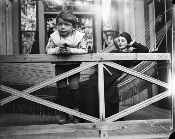 Syl and aunt Helen at Wild Rose cottage. Syl leans over the railing of the porch while Helen reclines in a hammock reading a book.