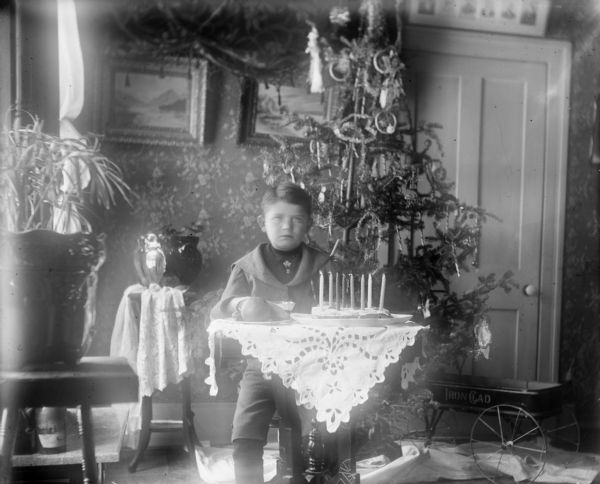 Syl sitting at a table with a birthday cake with eight candles. There is a Christmas tree in the background.